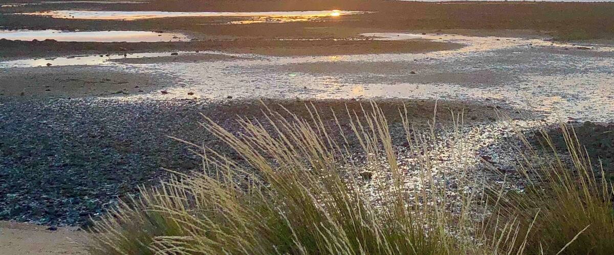 A sunset over a coastal landscape with a beach and distant mountains.