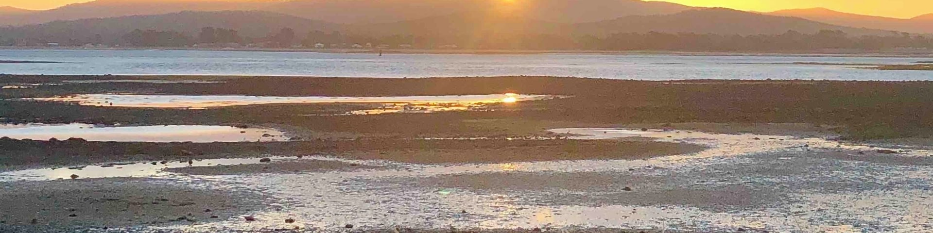 A sunset over a coastal landscape with a beach and distant mountains.