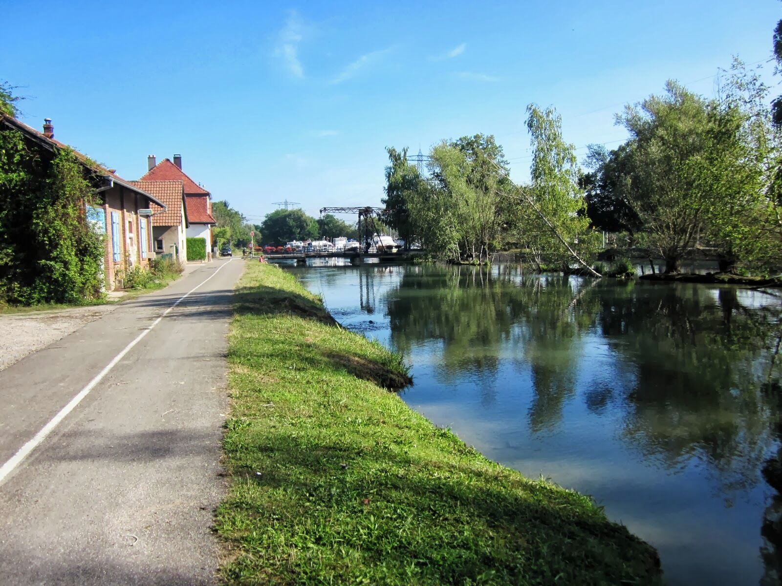A canal with a calm water surface, a road alongside, and buildings on the left.