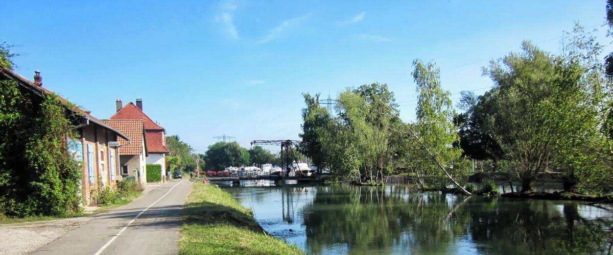 A canal with a calm water surface, a road alongside, and buildings on the left.