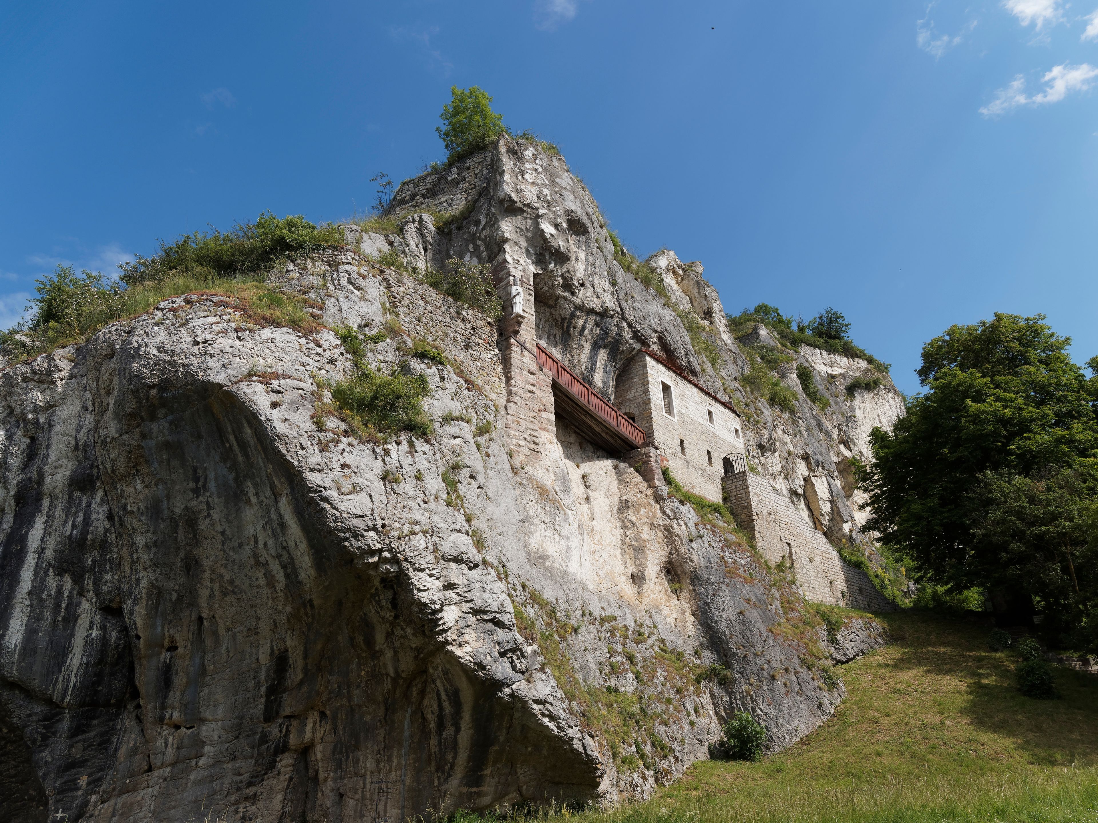 Un bâtiment en pierre, perché au sommet d’une falaise, avec un balcon rouge.