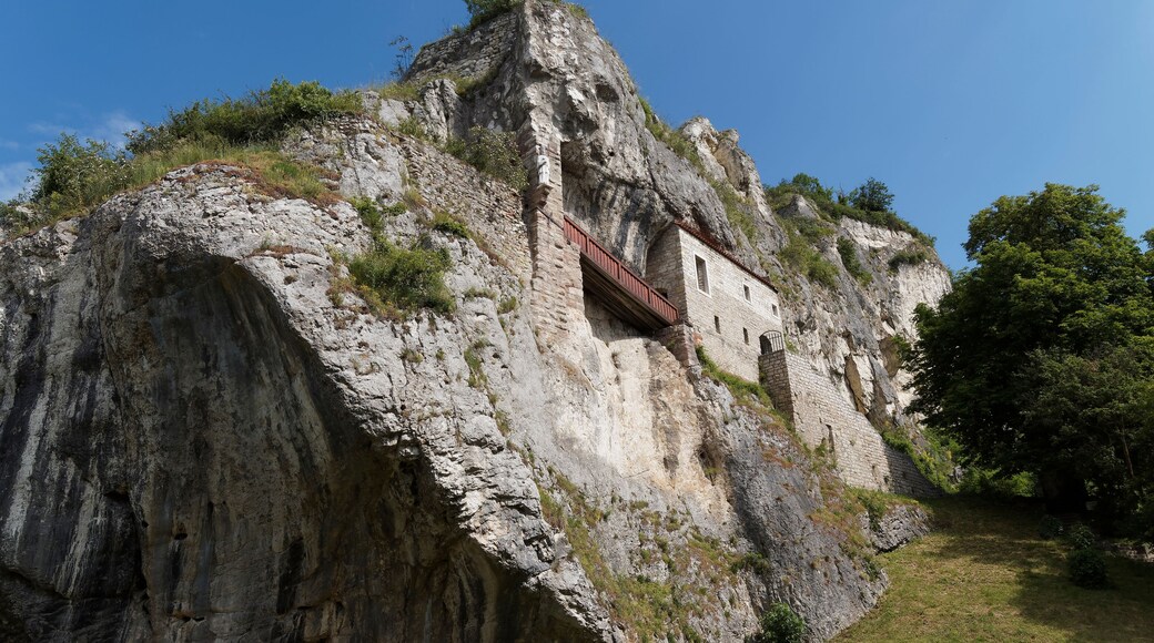 Un bâtiment en pierre, perché au sommet d’une falaise, avec un balcon rouge.