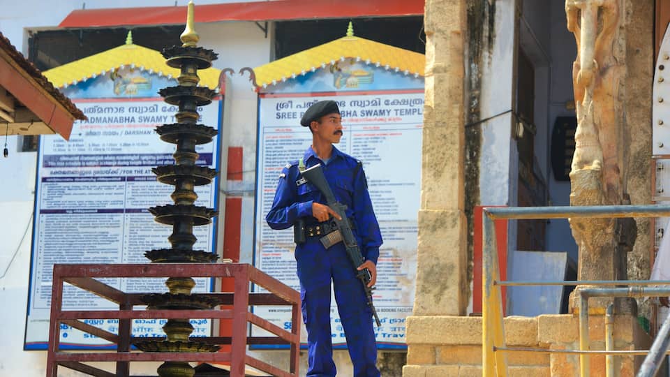 A security guard in blue uniform standing next to a traditional Indian lamp.