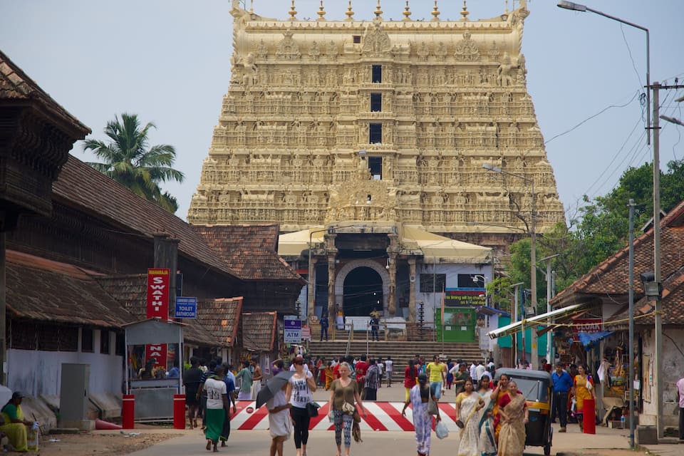 A large temple with intricate carvings, a busy street with people and shops, and traditional buildings.
