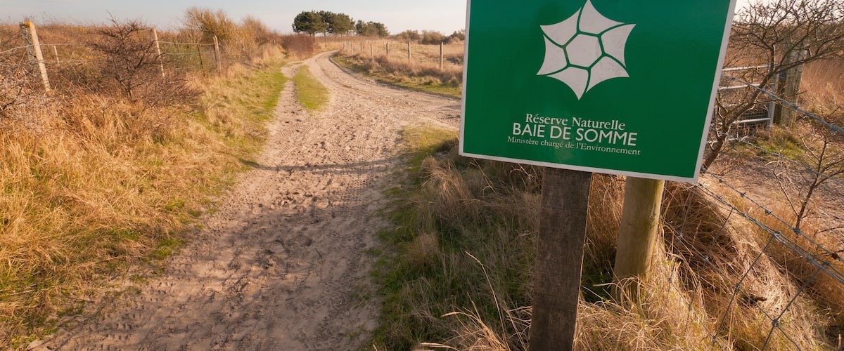 A dirt path leading through a natural area with a sign indicating a protected nature reserve.