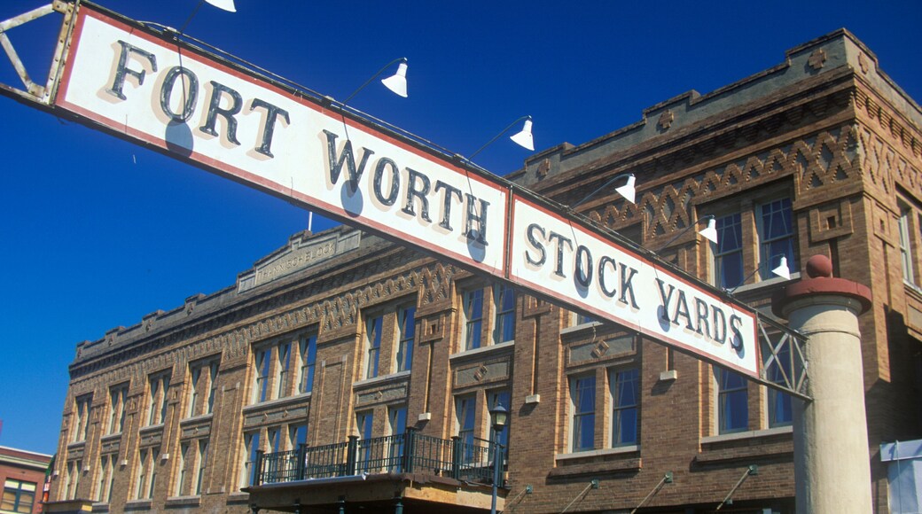 Een straatbord met de tekst 'FORT WORTH STOCK YARDS', met een historisch gebouw op de achtergrond.