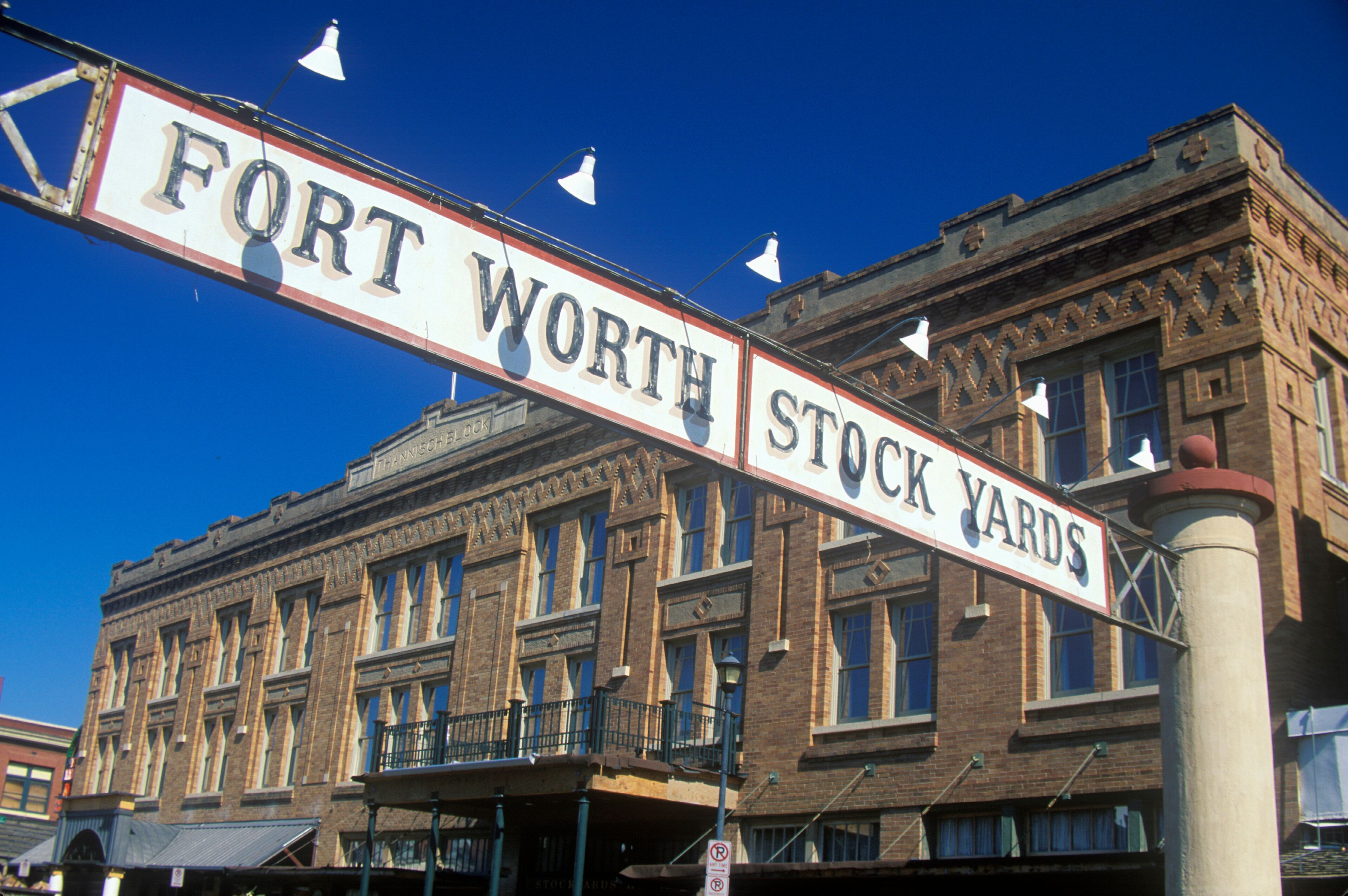 A street sign reading 'FORT WORTH STOCK YARDS' with a historic building in the background.