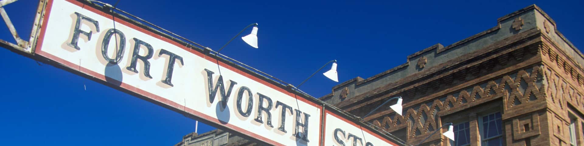 A street sign reading 'FORT WORTH STOCK YARDS' with a historic building in the background.