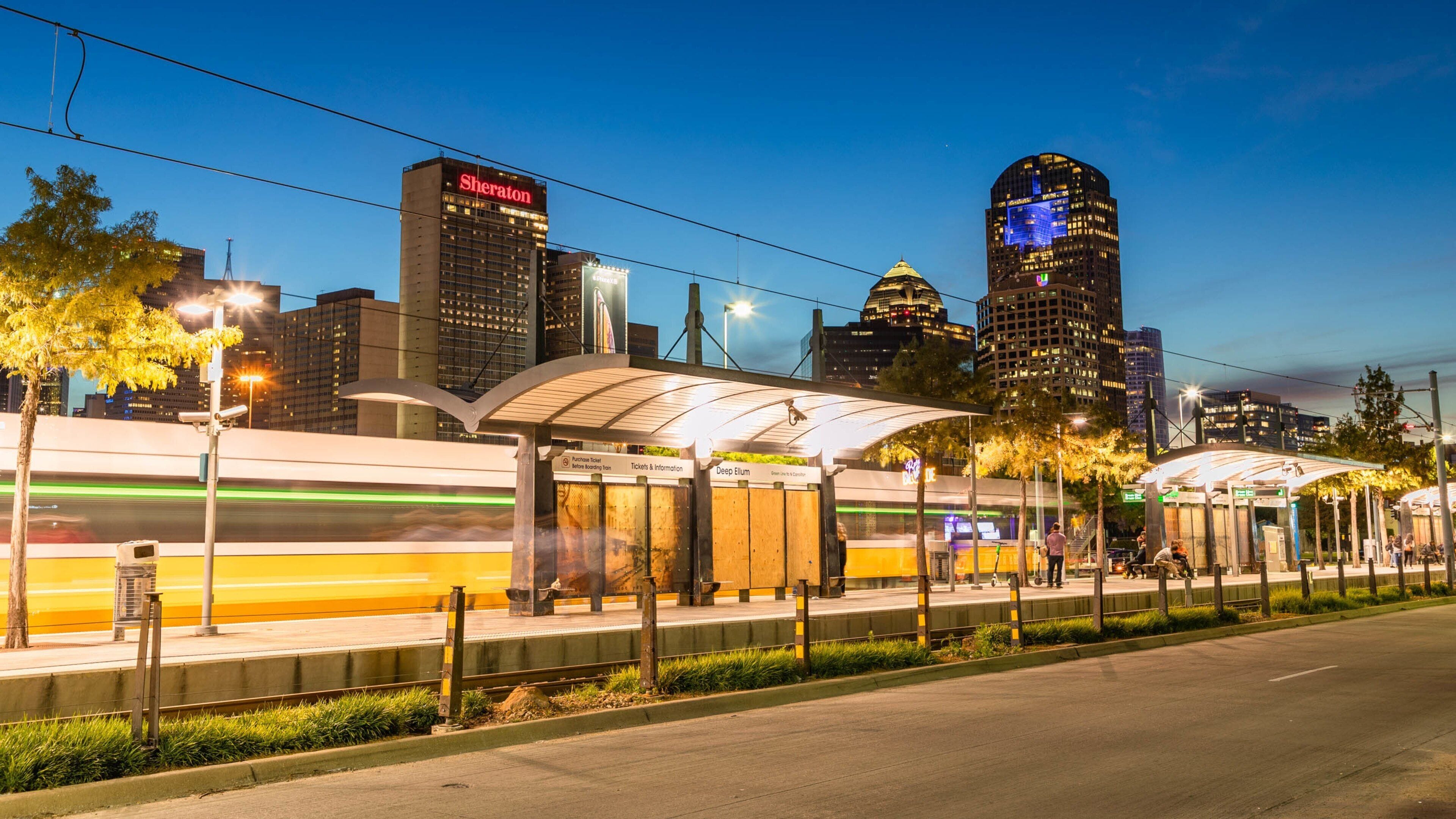 A train station with a modern design, a high-rise building with a 'Sheraton' sign, and a cityscape with illuminated skyscrapers.