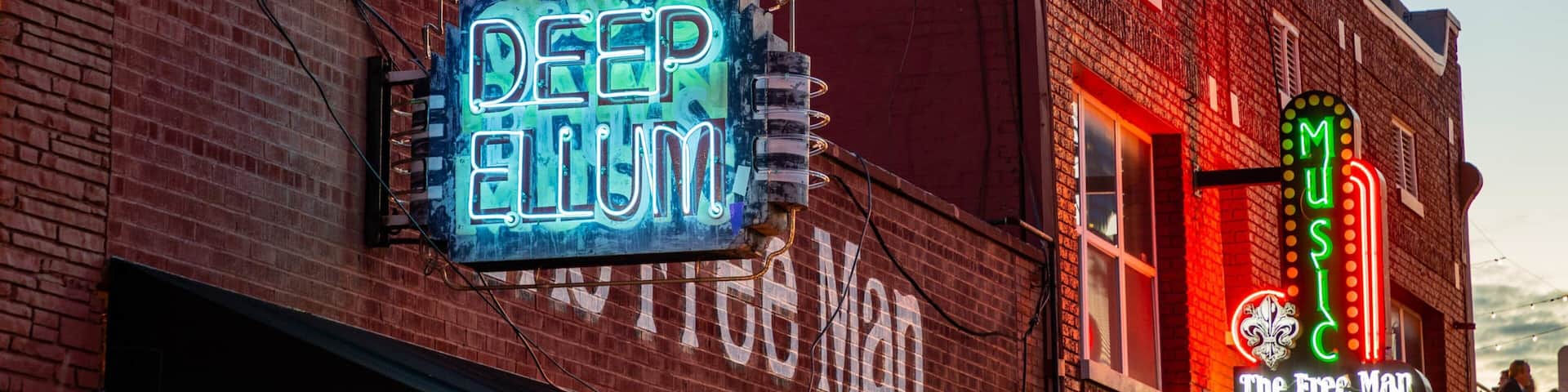 A brick building with neon signs for 'Deep Ellum' and 'The Free Man'.