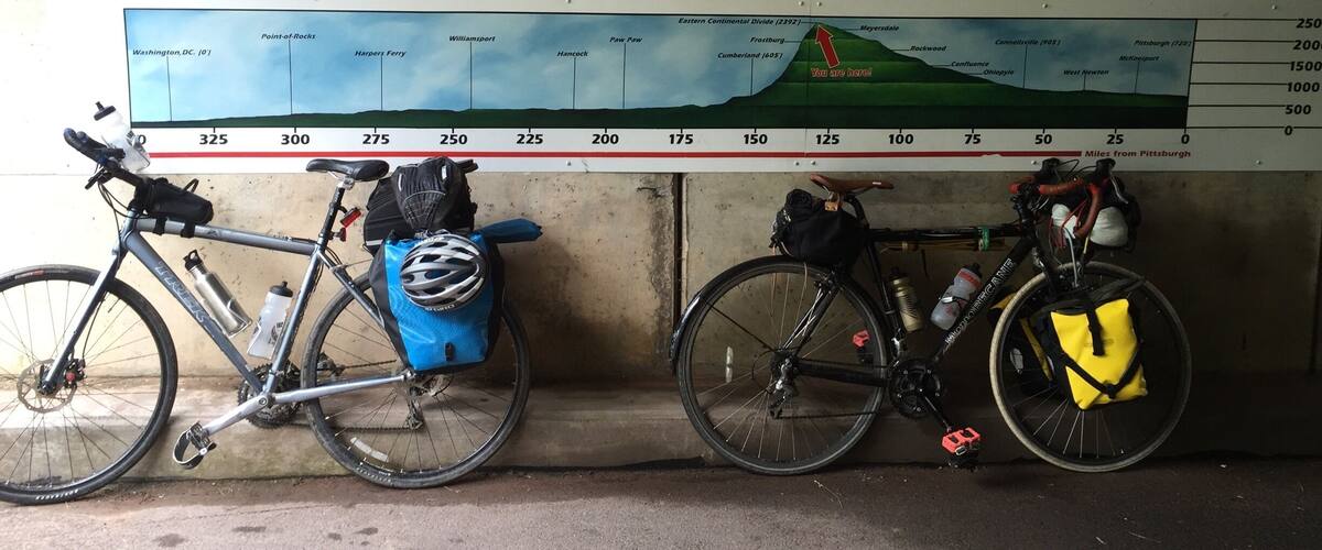 Two bicycles parked against a wall with a map of a cycling route.