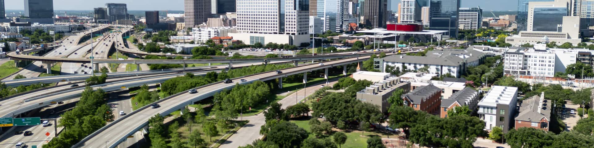 Dallas skyline with highway and greenspace of Griggs park with State Thomas Uptown neighborhood on beautiful day.