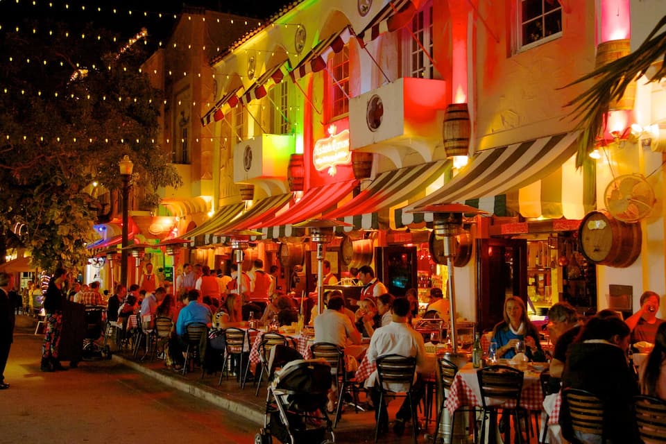 A bustling street lined with brightly lit restaurants and outdoor seating areas.