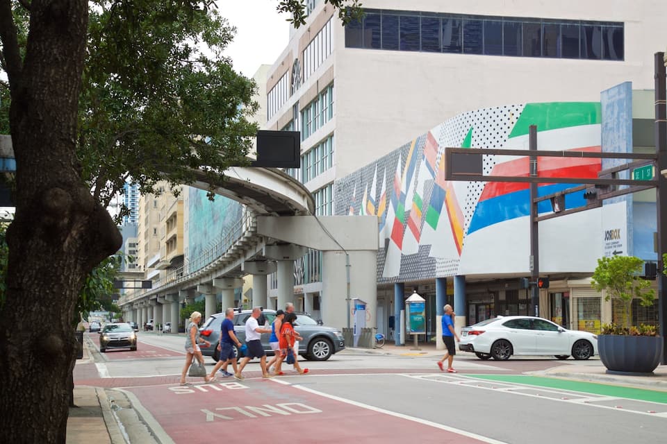 Un carrer urbà amb un carril bus, vianants, cotxes i un edifici amb un mural de colors.