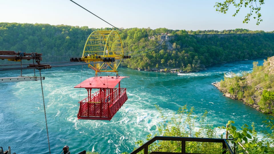 A cable car system over a river with a red gondola, surrounded by lush greenery and rocky cliffs.