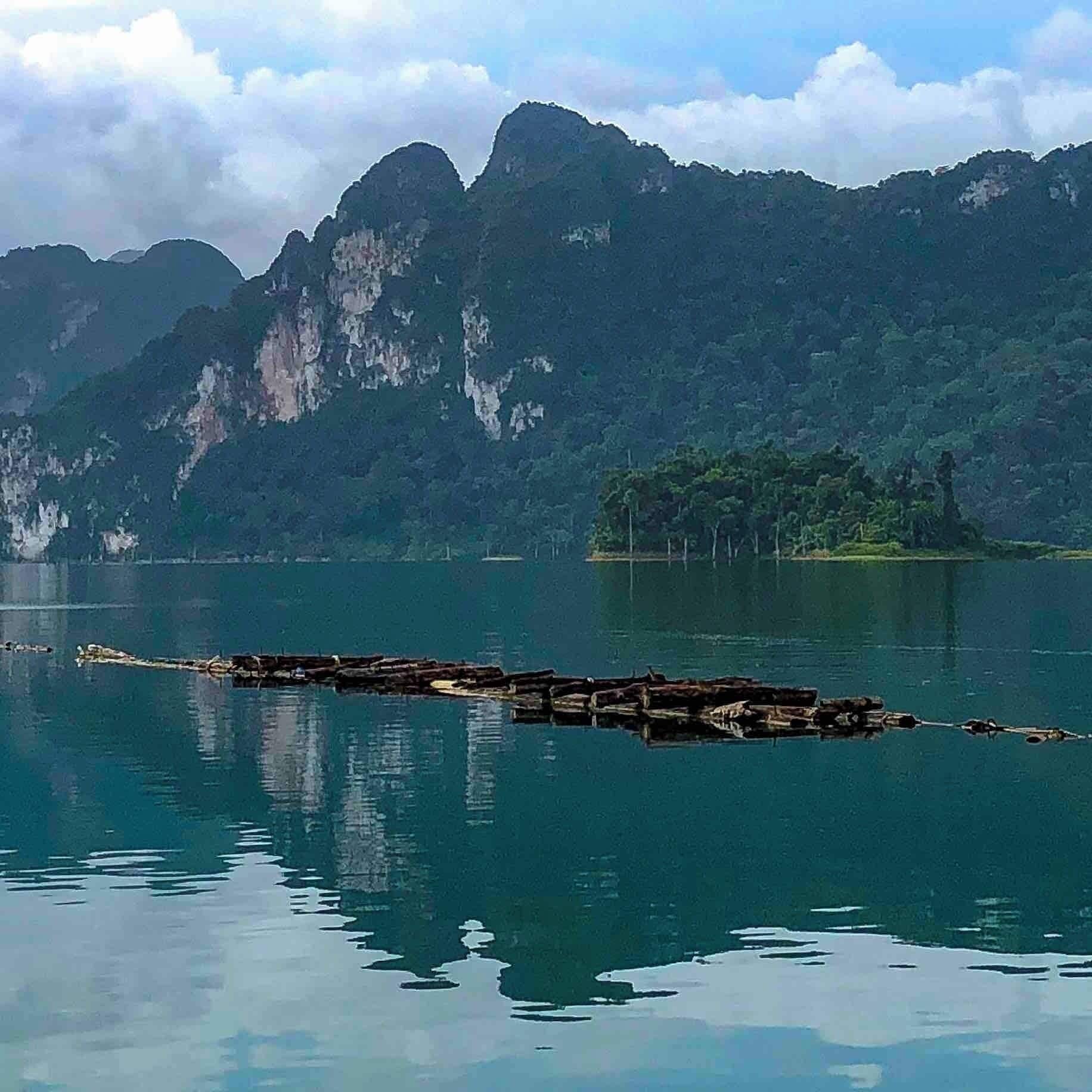 Un lago tranquilo con un muelle de madera que se adentra en el agua, rodeado de exuberantes montañas verdes y un cielo despejado.