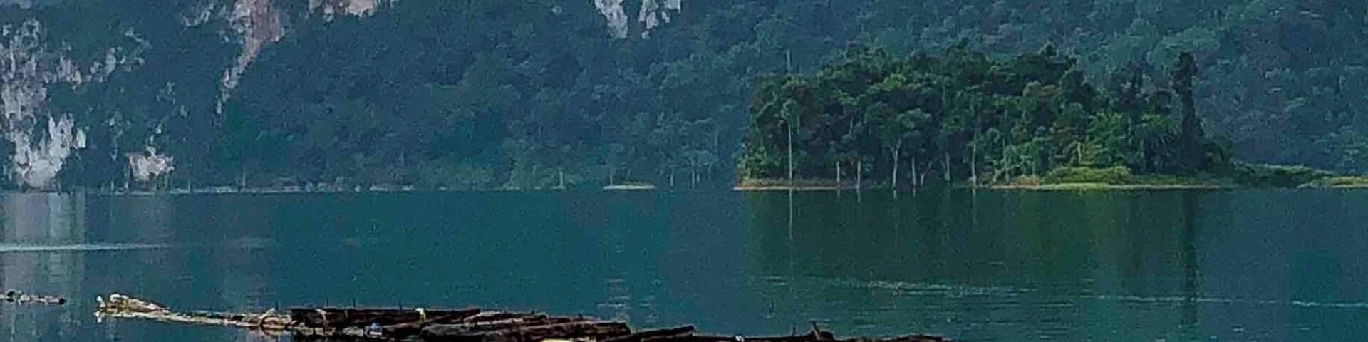 Un lago tranquilo con un muelle de madera que se adentra en el agua, rodeado de exuberantes montañas verdes y un cielo despejado.