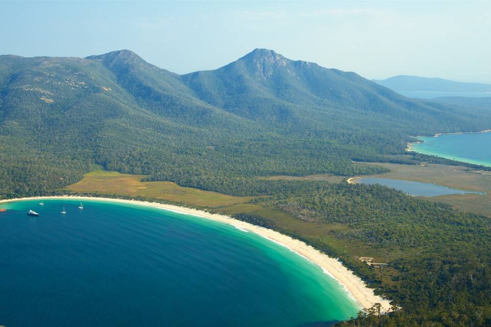 A coastal landscape with a turquoise beach, clear blue waters, and a backdrop of green mountains.