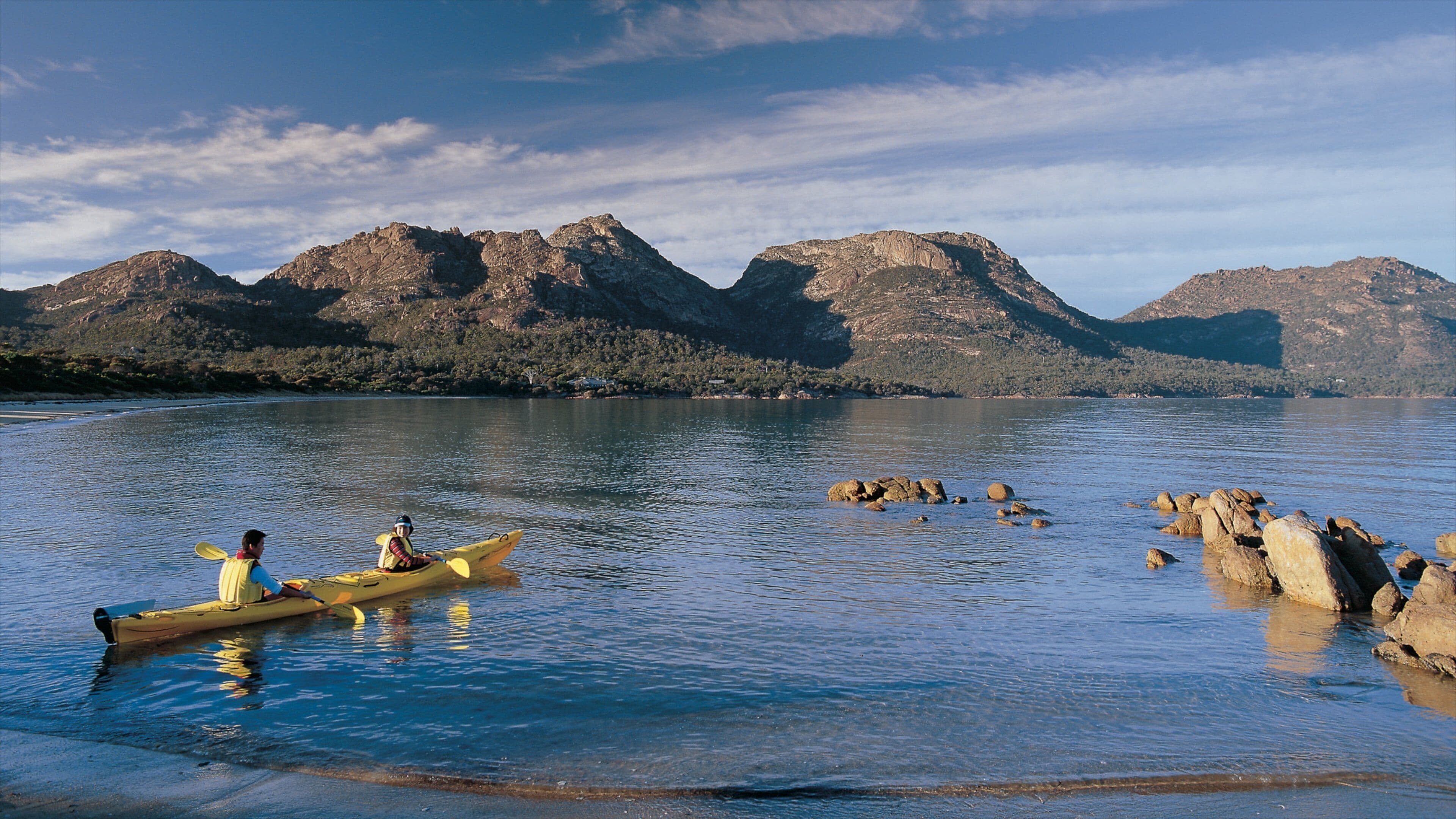 A calm lake with a kayak and a person paddling, surrounded by rocky mountains.