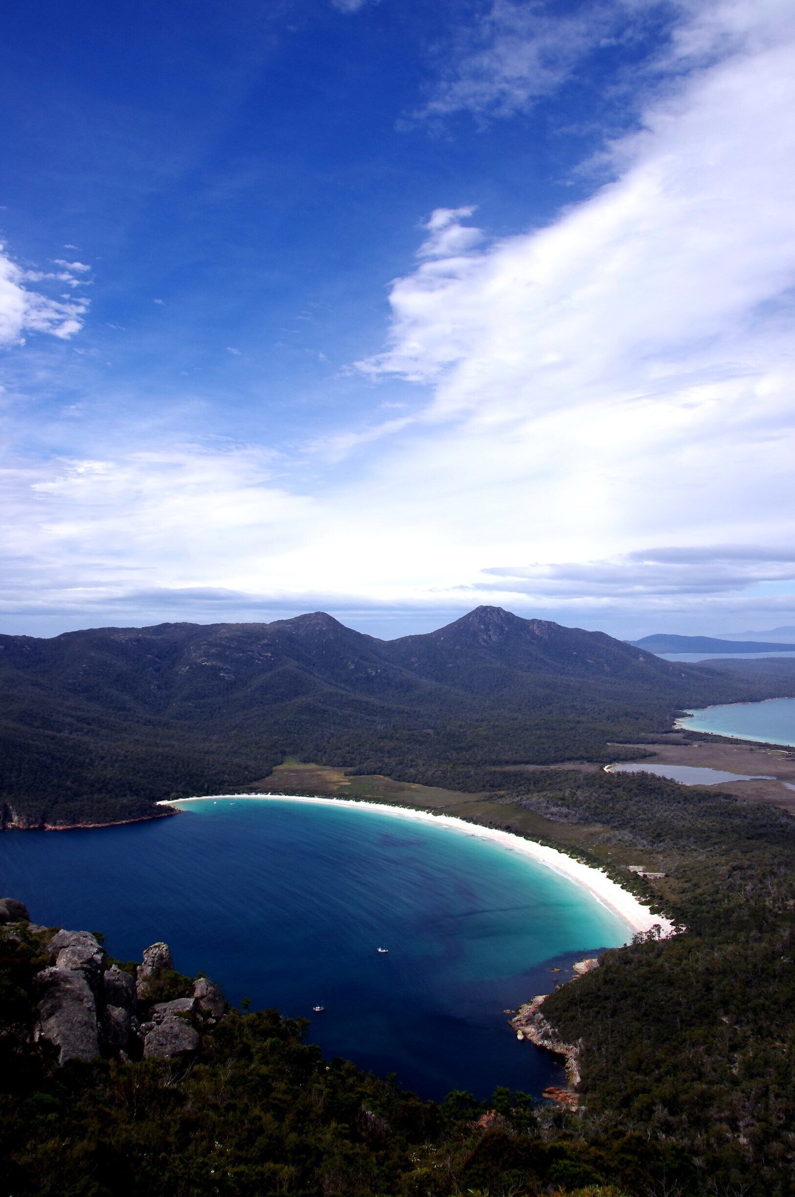 A coastal landscape with a turquoise bay, surrounded by mountains and dense forests.