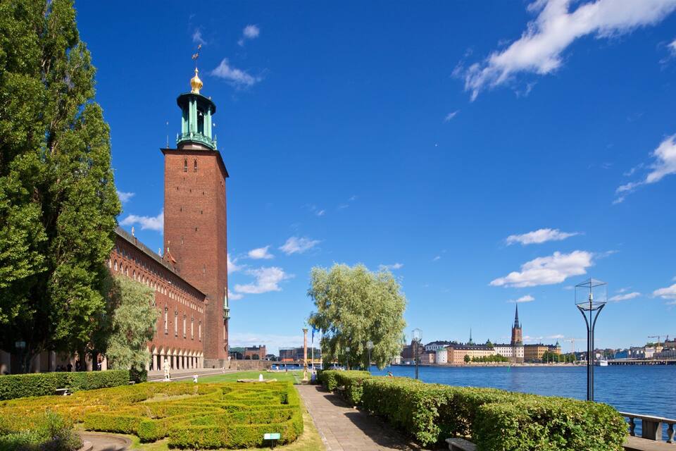 A historic tower with a spire, a river, and a cityscape in the background.