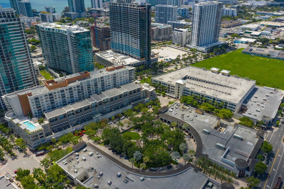 Vista aérea de un paisaje urbano con edificios modernos de gran altura, un amplio estacionamiento y un área verde de parque.