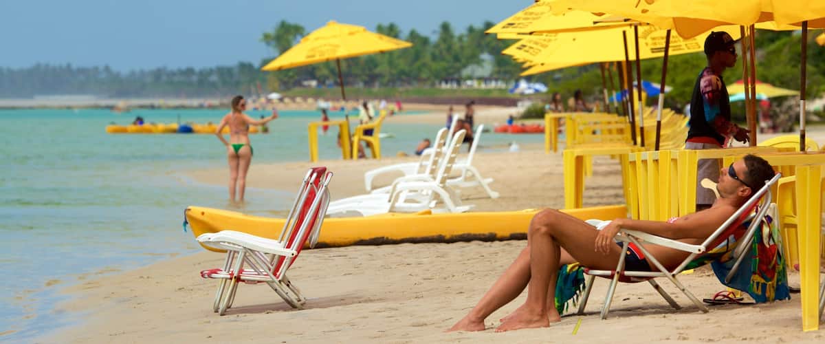 A beach with yellow umbrellas, white lounge chairs, and people relaxing.