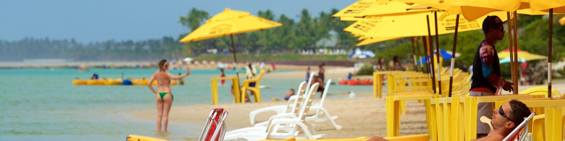 A beach with yellow umbrellas, white lounge chairs, and people relaxing.