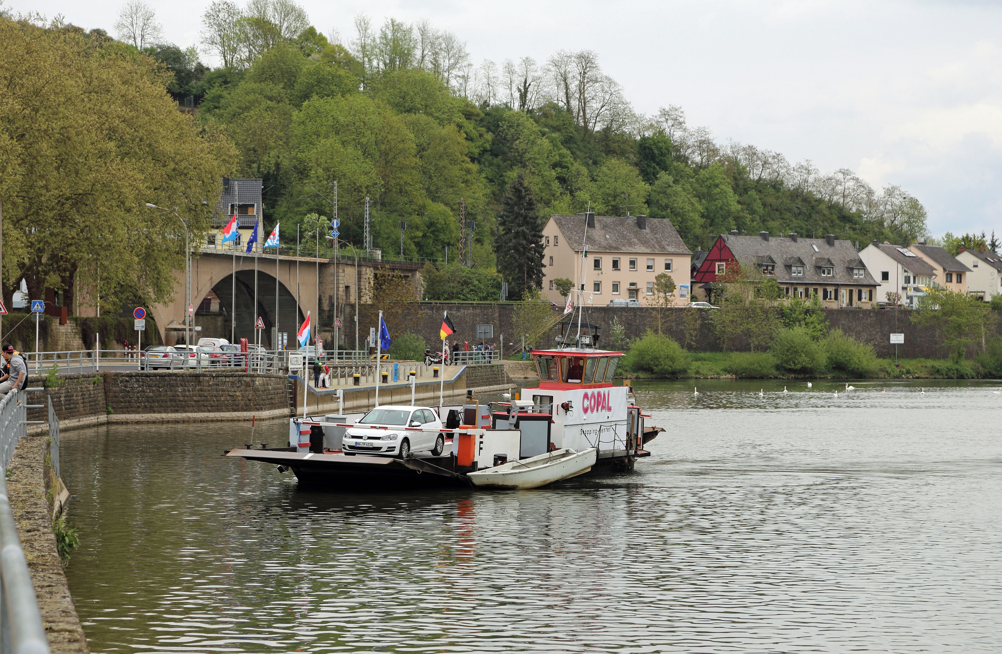 A river with a boat carrying cars, a bridge, and buildings in the background.