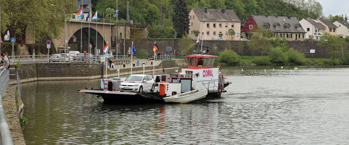 A river with a boat carrying cars, a bridge, and buildings in the background.