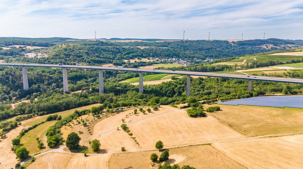 A bridge over a valley with solar panels and wind turbines in the background.