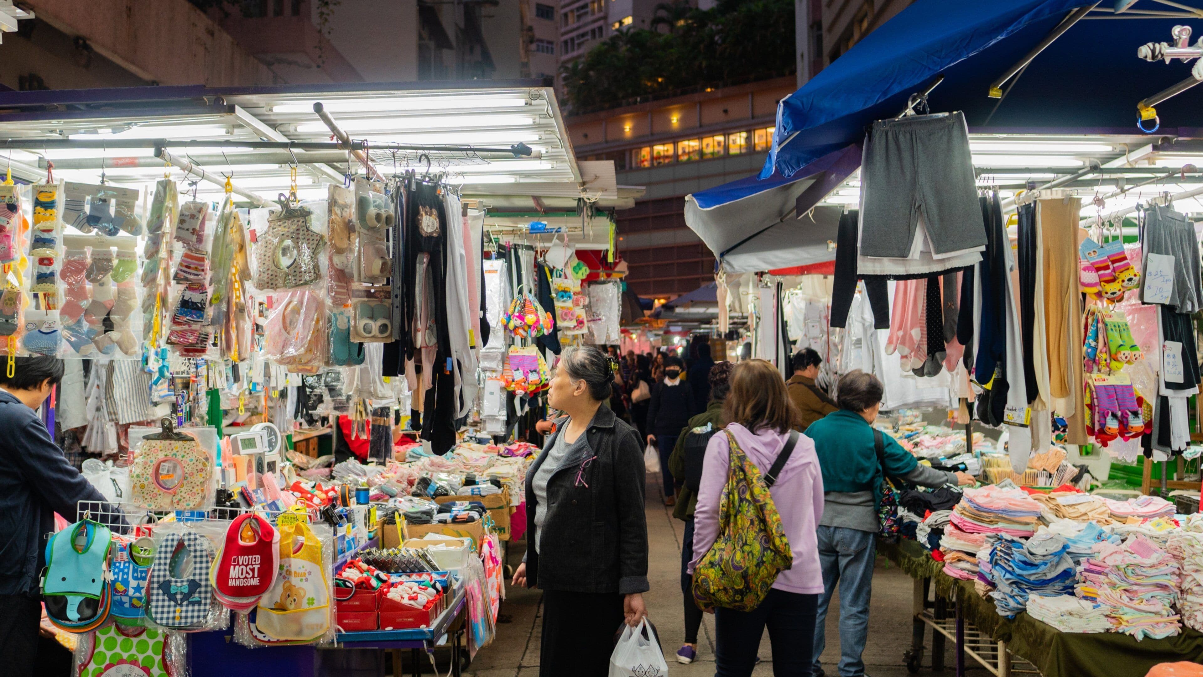 A bustling outdoor market with various stalls selling clothing, accessories, and household items.