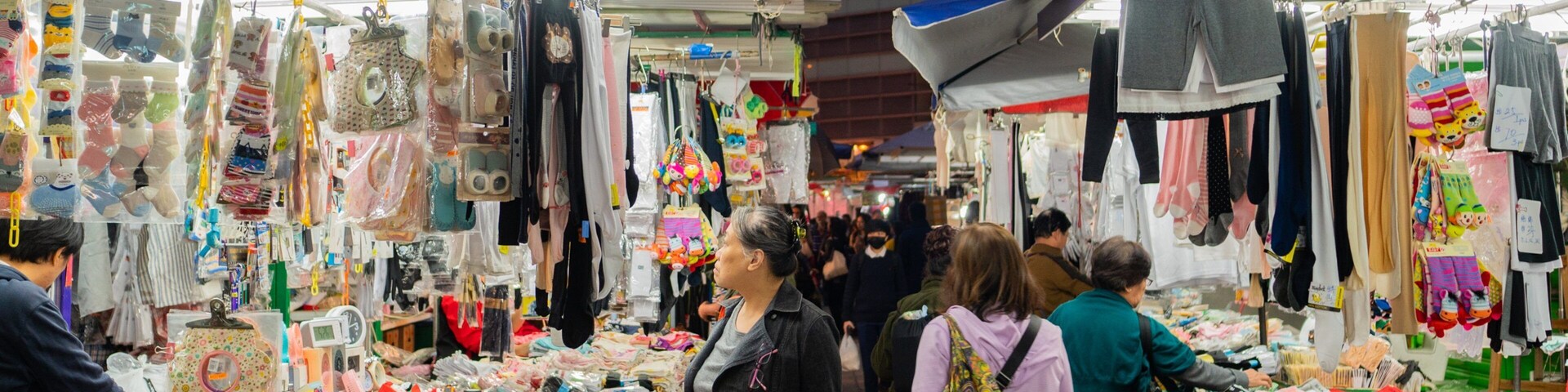A bustling outdoor market with various stalls selling clothing, accessories, and household items.