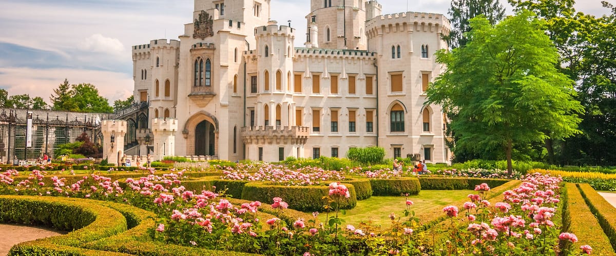 A castle with a tower, surrounded by a formal garden with pink flowers.