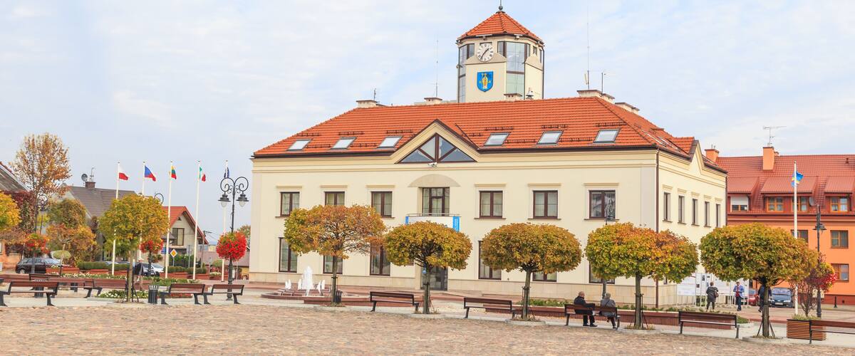 A historic building with a clock tower, surrounded by a cobblestone plaza and autumn trees.