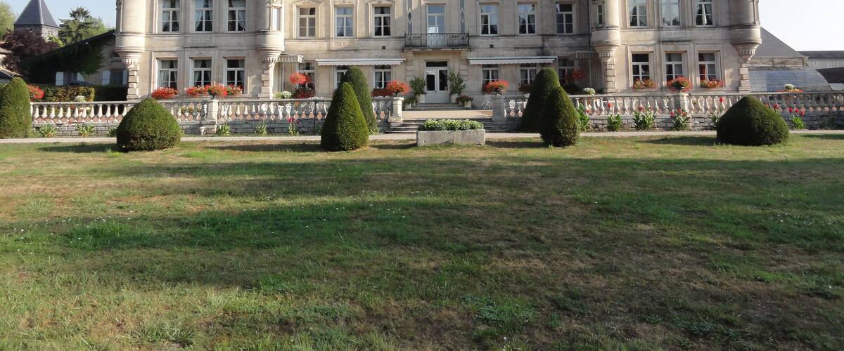 A large, historic building with multiple towers and a well-maintained garden.