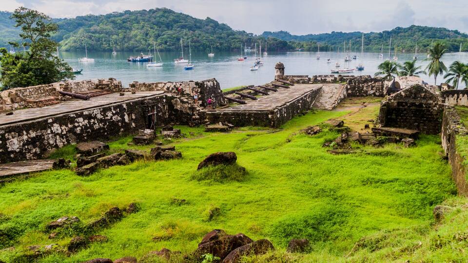 A historic fort with lush green grass and palm trees in the background.