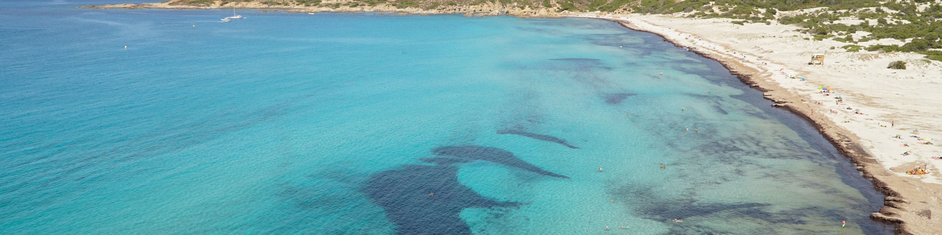 Un paysage cĂŽtier avec une eau turquoise cristalline, une plage de sable et des montagnes rocheuses en arriĂšre-plan.