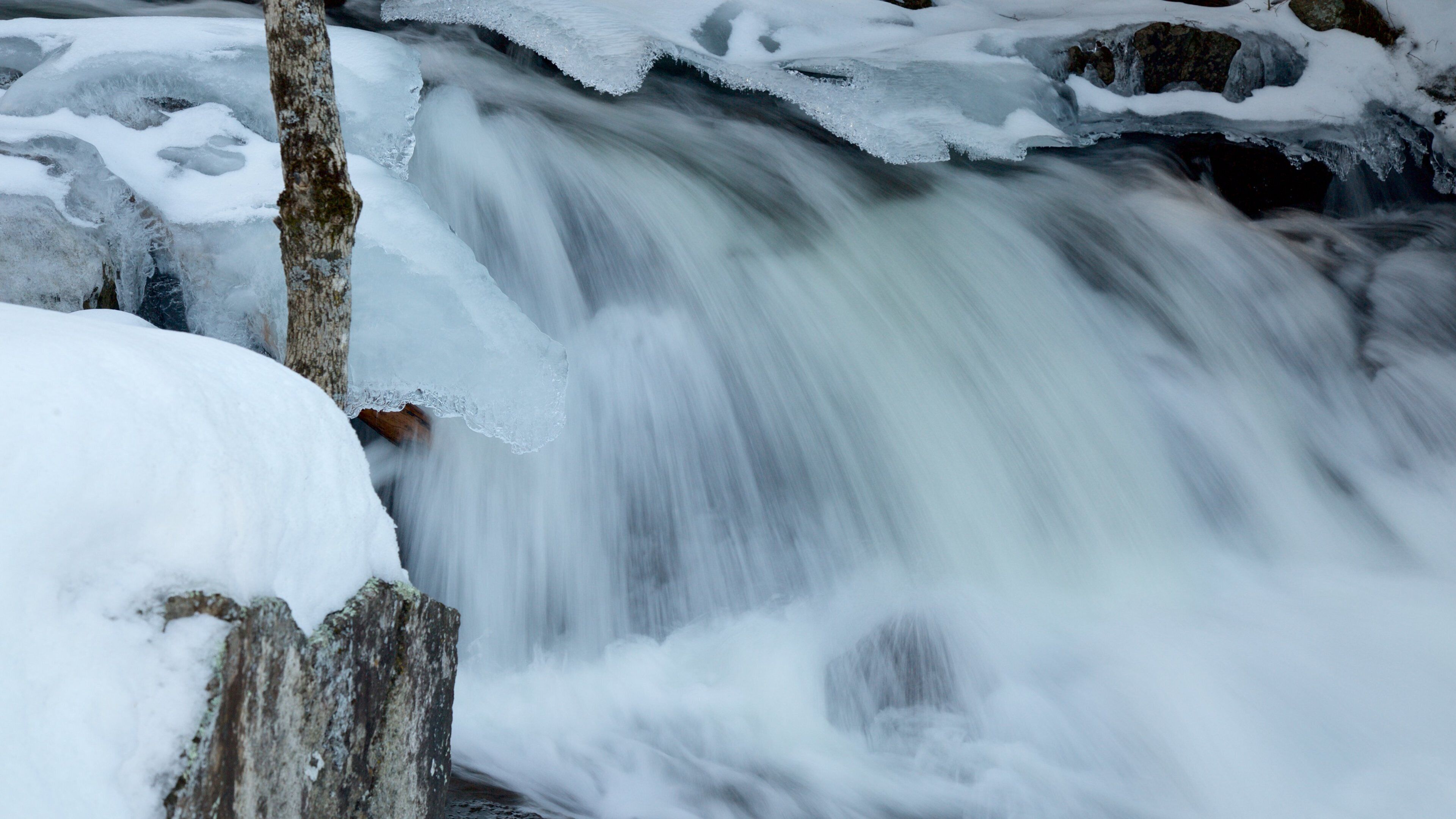 A frozen waterfall with ice formations and a tree trunk.