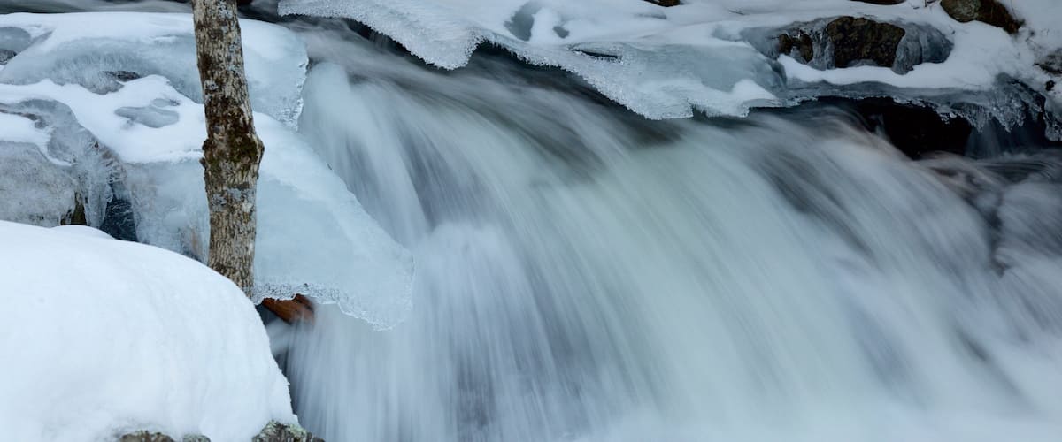 A frozen waterfall with ice formations and a tree trunk.