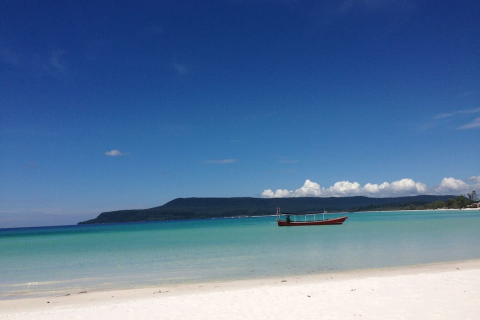 A boat on a turquoise beach with a mountain in the background.