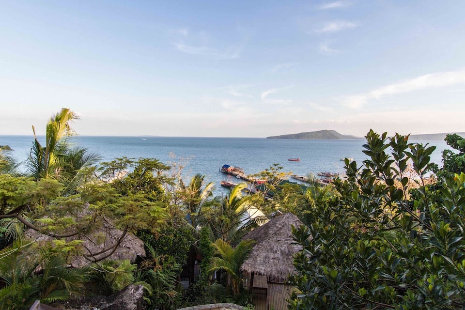 A tropical beach with boats, palm trees, and thatched huts.