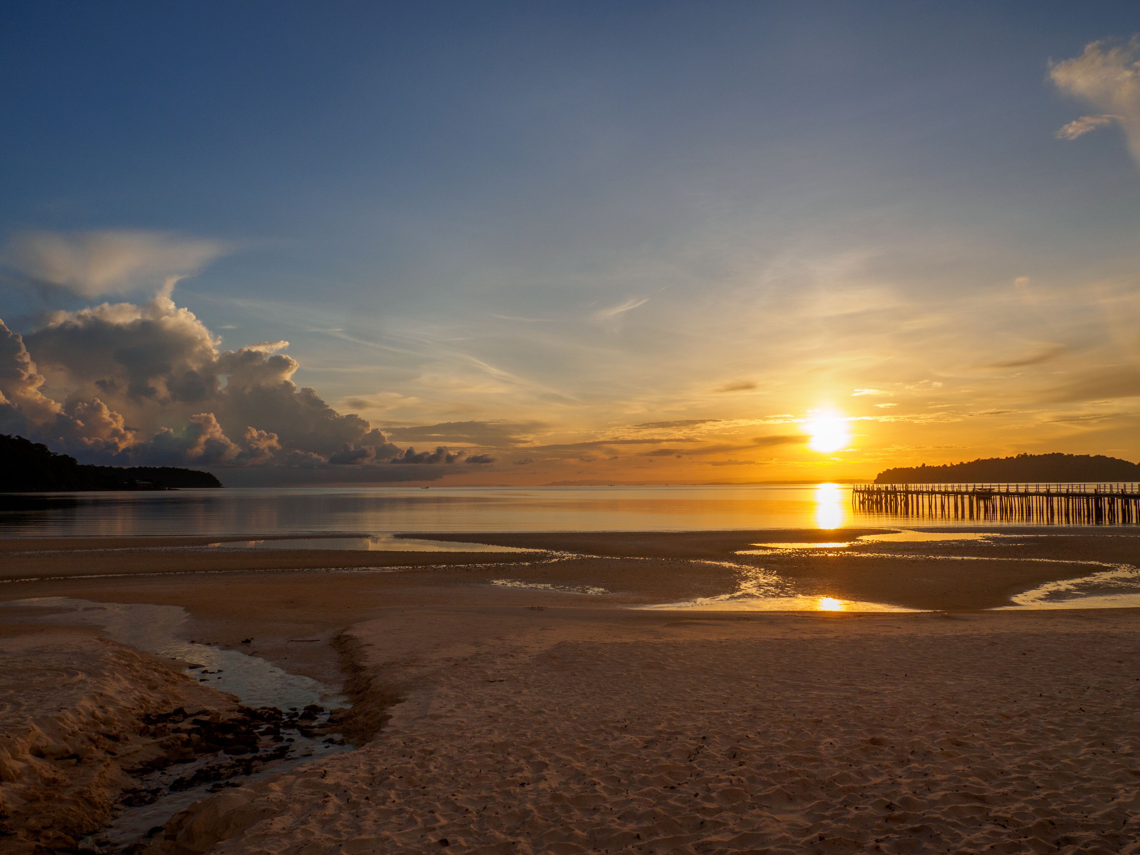 A beach at sunset with a pier extending into the water.