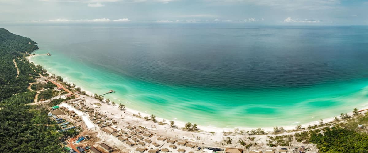 A coastal area with a turquoise bay, a sandy beach, and a road curving along the coastline.