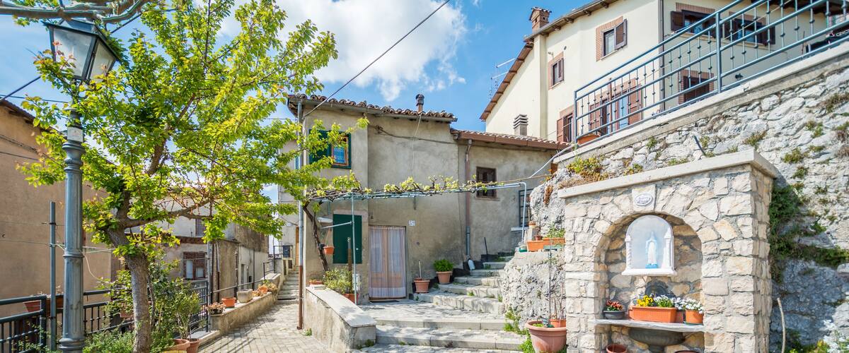 A cobblestone street with potted plants, a stone archway, and traditional buildings.