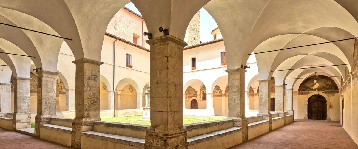 A courtyard with arches, stone columns, and a brick floor.