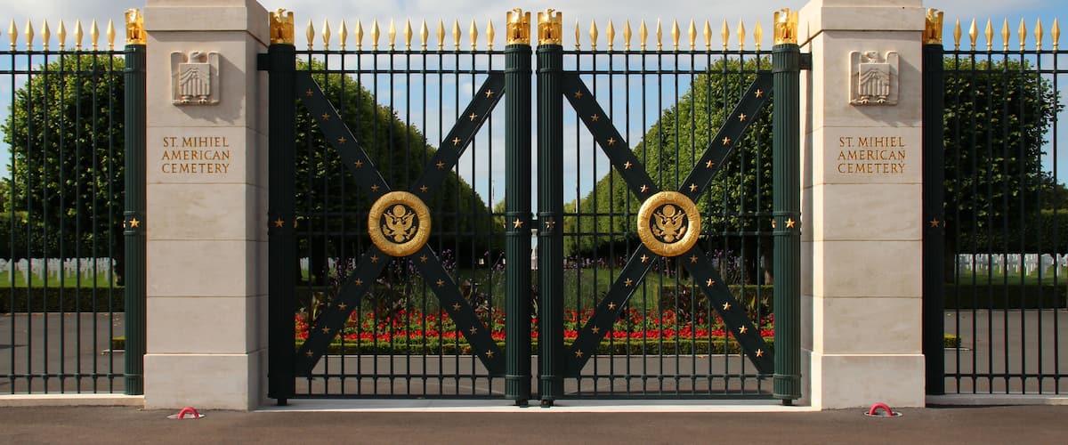 A gated entrance to St. Michael American Cemetery with a double gate and a clear sky.