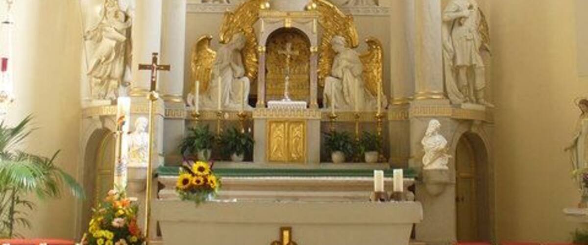 An ornate church interior with a central crucifix, statues, and a golden halo above the altar.