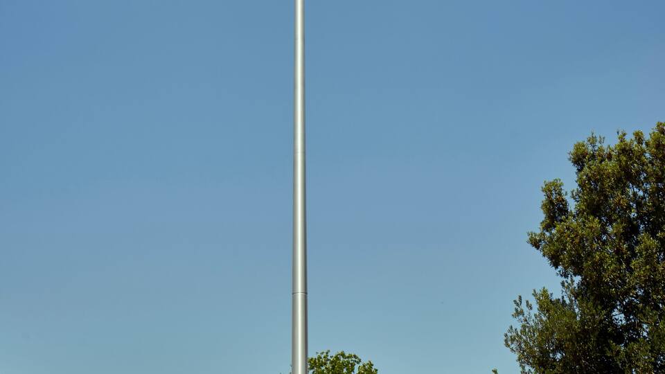 Eine Fahnenstange mit einer Regenbogenflagge vor blauem Himmel.