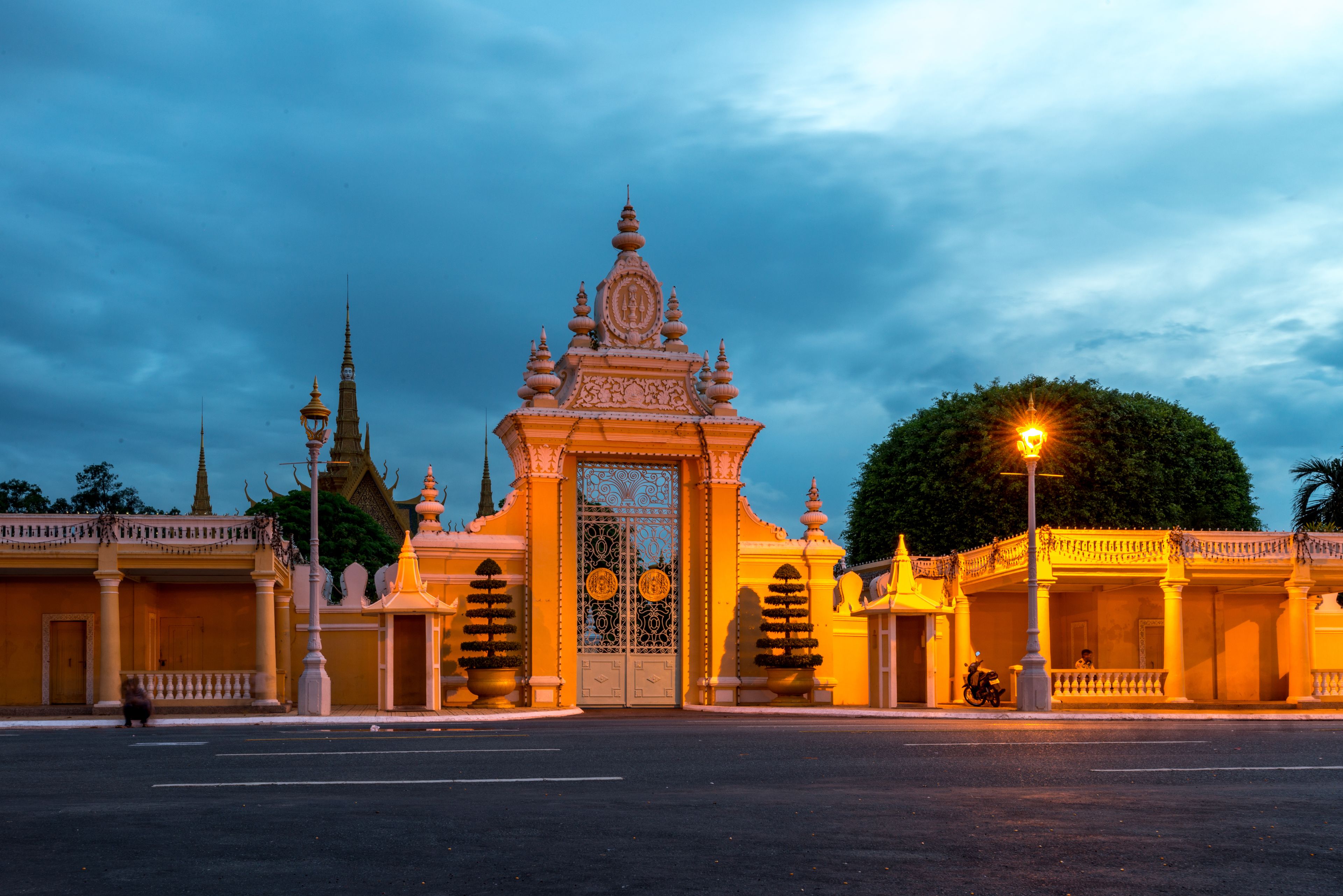 A temple with ornate architecture and a large gate, surrounded by a well-maintained garden and a clear sky.